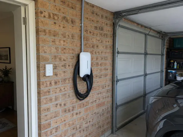 Wall-mounted EV charger on a brick garage wall beside a doorway and roller door in Lakelands