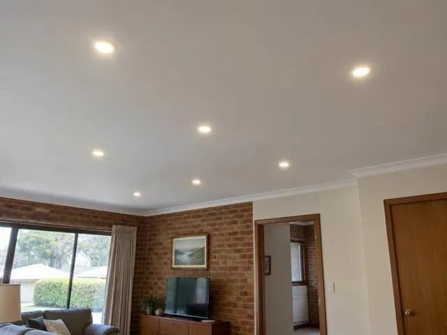 Ceiling downlights in a living room with brick feature wall and window in Eleebana
