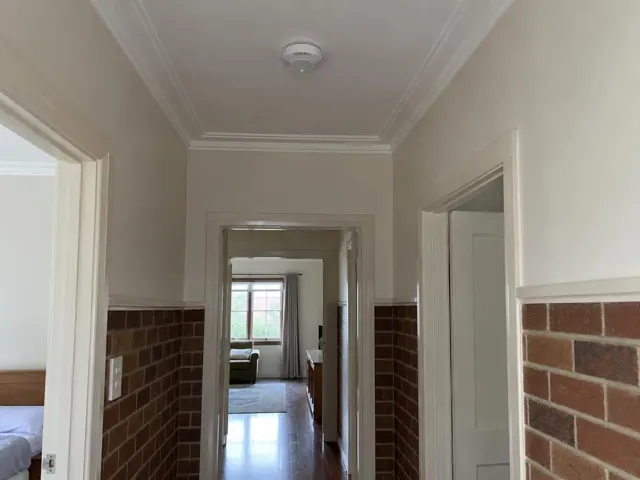 Ceiling smoke alarm in a tiled hallway with doorways and crown moulding in Boolaroo